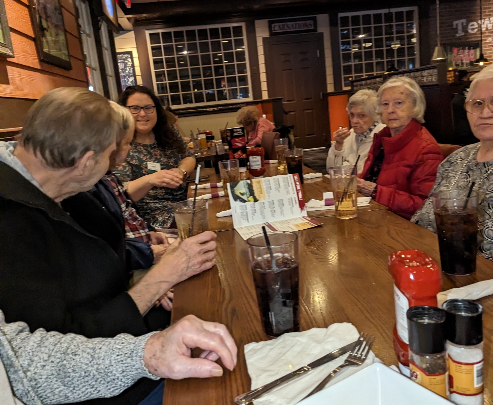 A caregiver smiling at a restaurant table with a group of older women enjoying dinner out together.